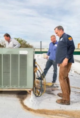 Three HVAC technicians on a flat Phoenix-area roof beside a rooftop package unit, with Tom Mattingly in a navy work shirt standing at right